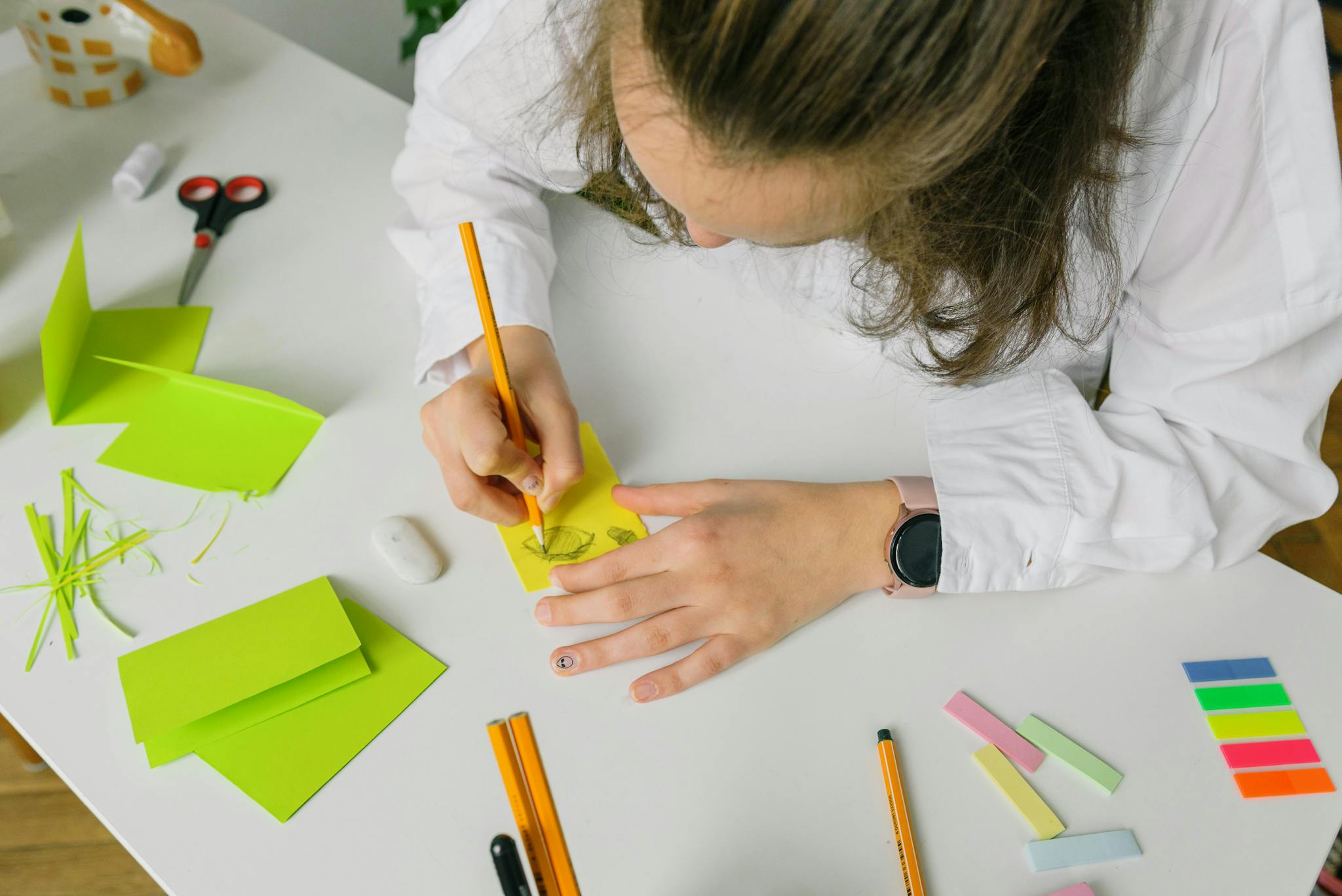 Top view of a person sketching on a desk with colorful craft materials, focusing on creativity and design.