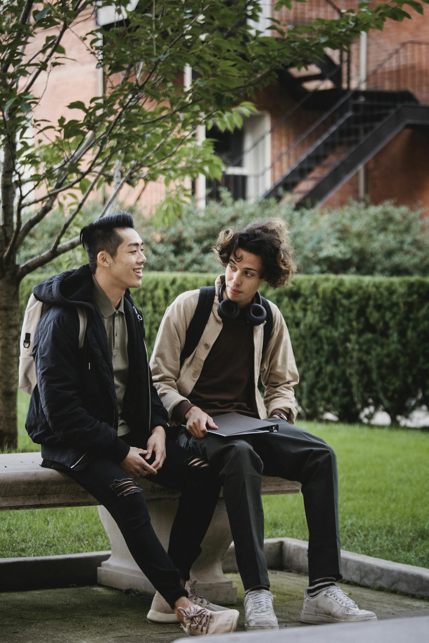 Two young men sitting on a bench talking and enjoying campus life outdoors.